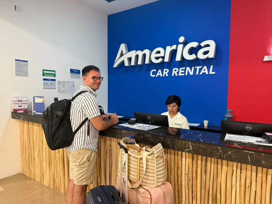 Yo en el mostrador de alquiler de coches en Tulum